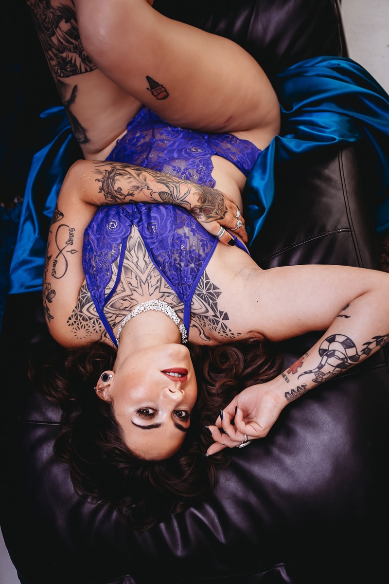 Lady in blue outfit laying on a leather couch looking up at the camera