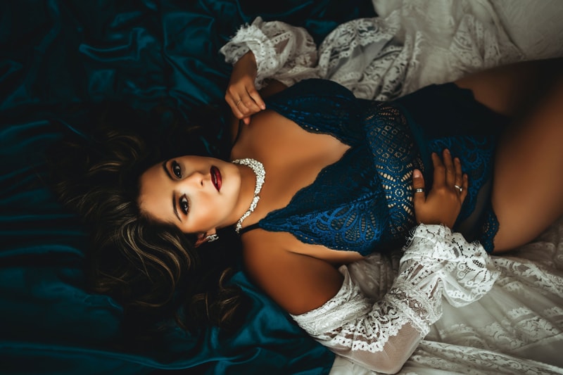 Lady in blue outfit laying on silk sheets with white lace rope