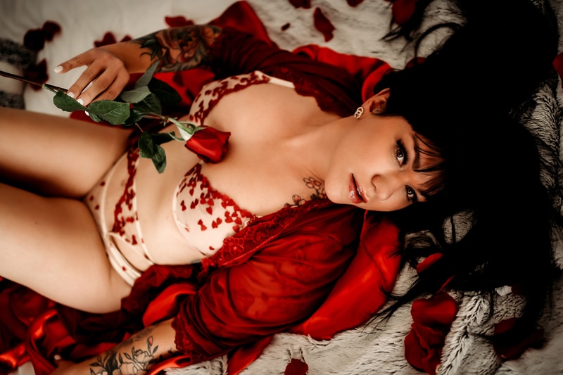 Lady wearing see thru bra with hearts and red rope holding a rose  looking at camera