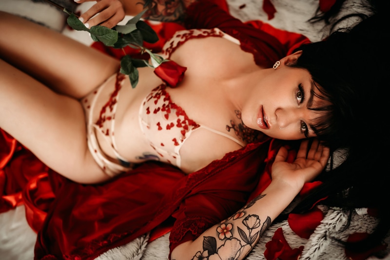 black haired lady laying in a red robe with hearts all over it and shes holding a robe