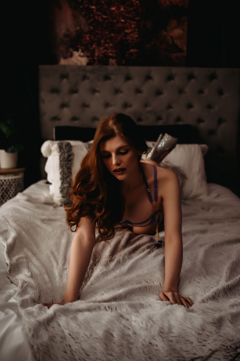Red haired lady laying on bed with fuzzy blanket looking at her hands