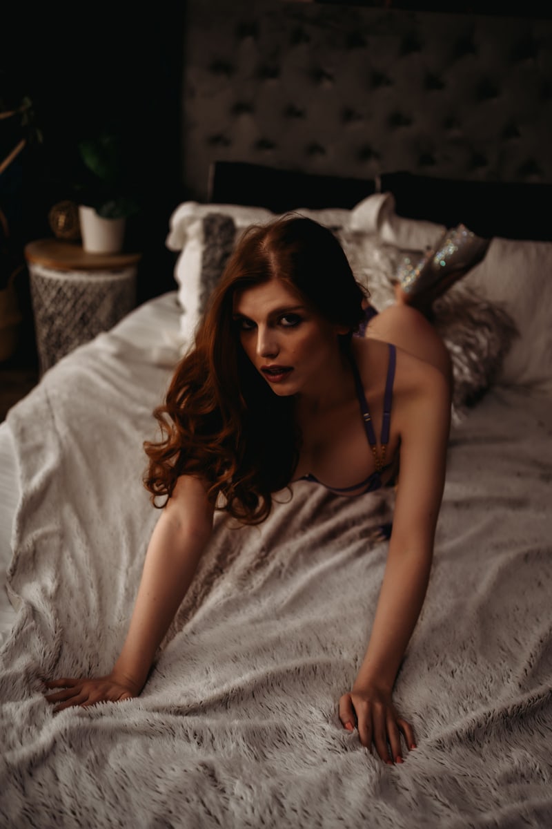 red haired lady laying on bed looking at camera on fuzzy blanket wearing sparkly heels