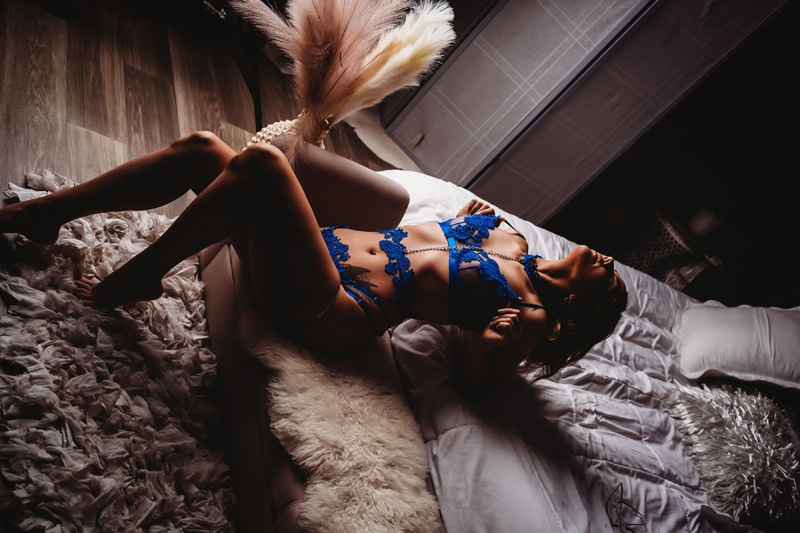 boudoir shoot of a wearing blue lingerie, she is doing a pose on a bed, and the picture is moody