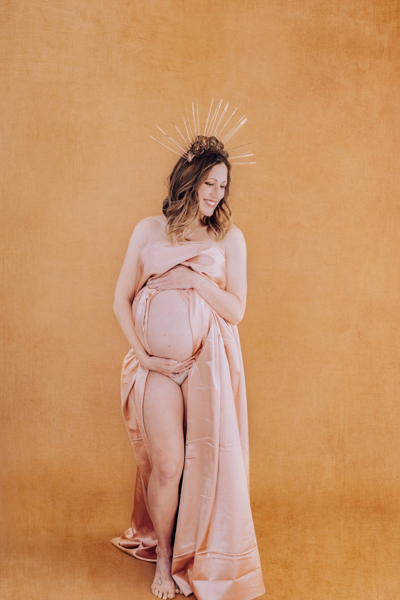Pregnant woman holding belly in oink drape boudoir shoot
