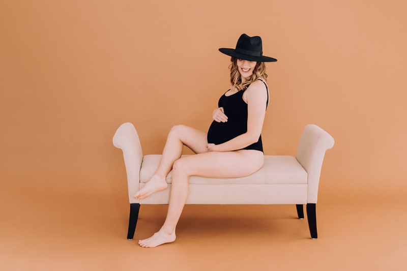 Pregnant woman in black body suit on bench boudoir sessions